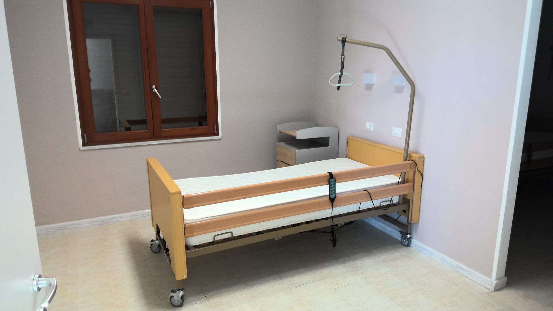Camera d'ospedale con un letto singolo regolabile, comodino e apparecchiature mediche a parete.