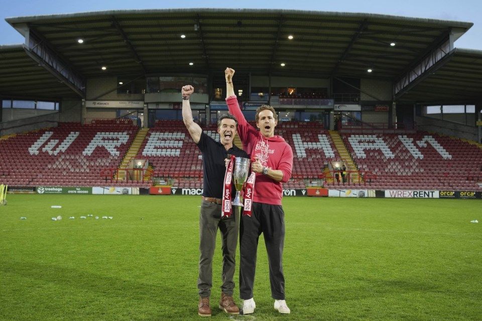 Two men are standing on a soccer field with their arms in the air.