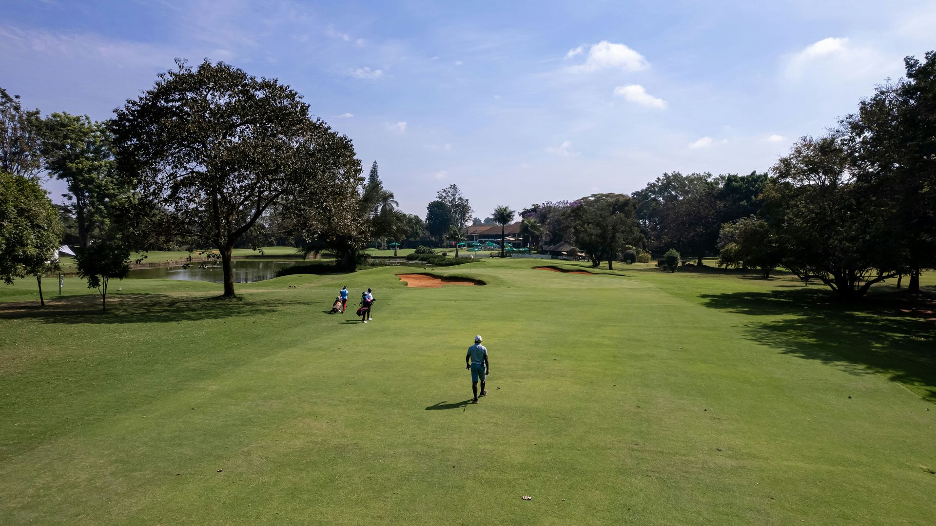 Golf course scene with golfers on the fairway under a bright sky.