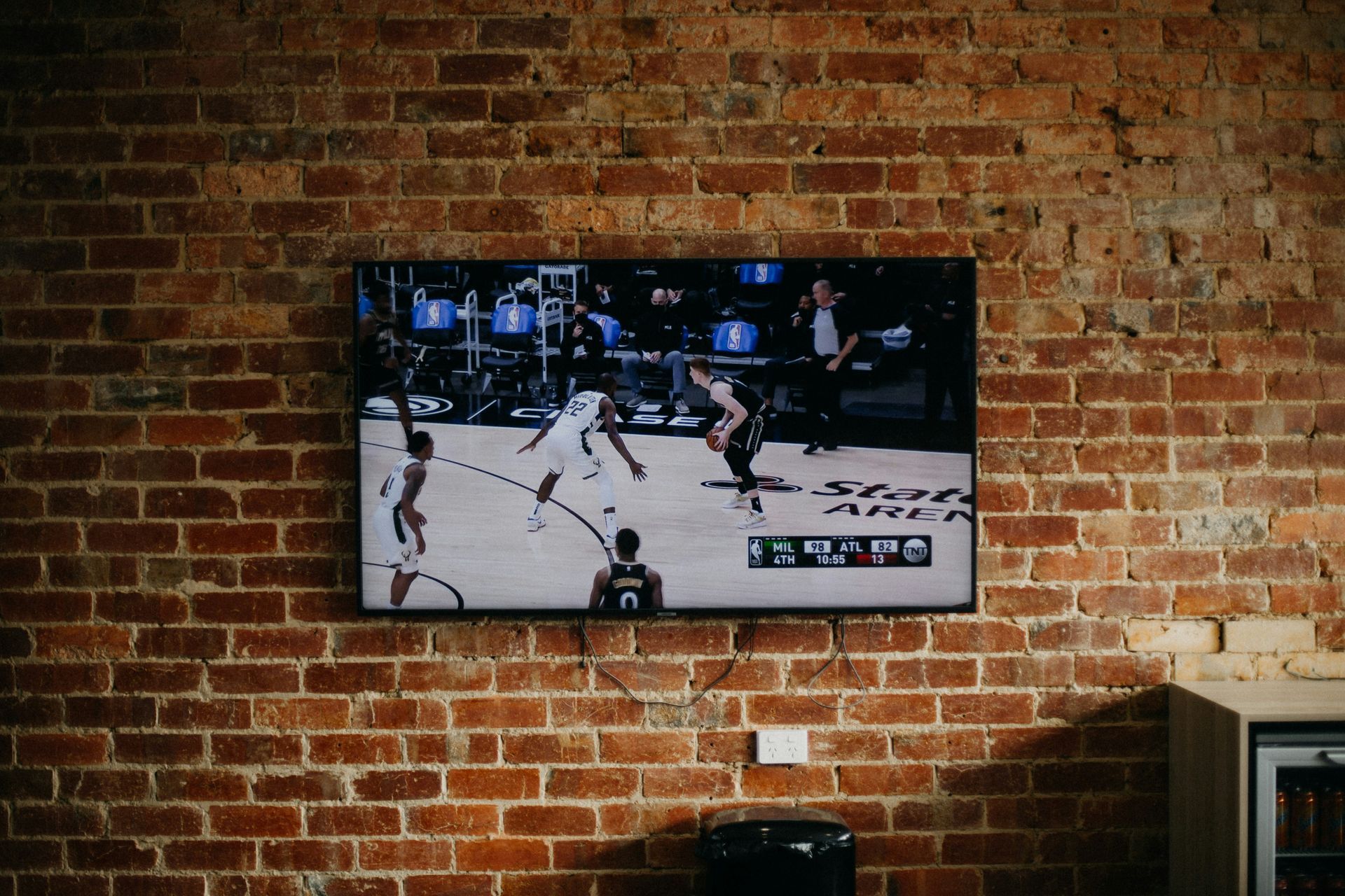 Television showing a basketball game on a brick wall.
