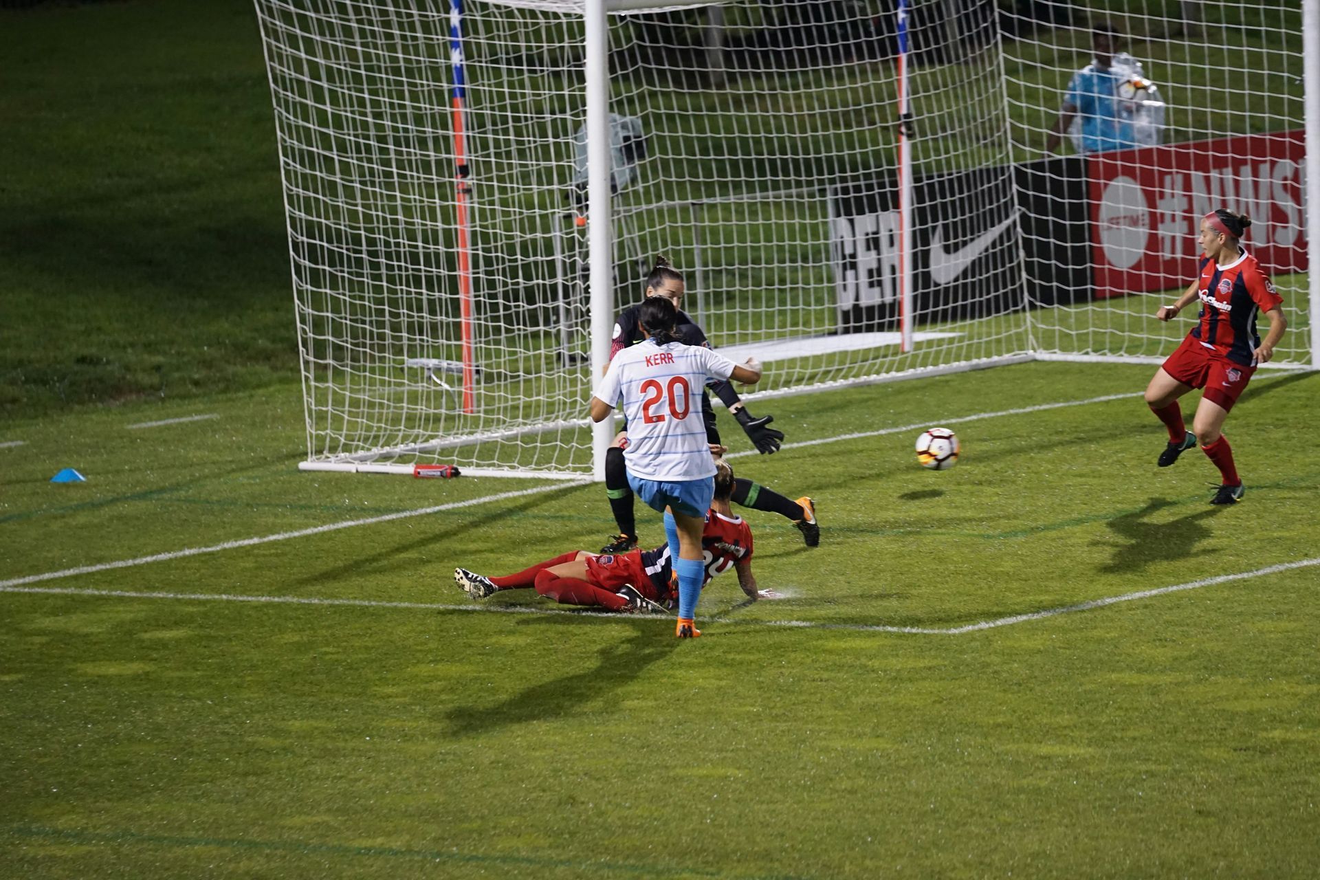 Soccer game: Player in white jersey scores a goal; goalie dives near net.