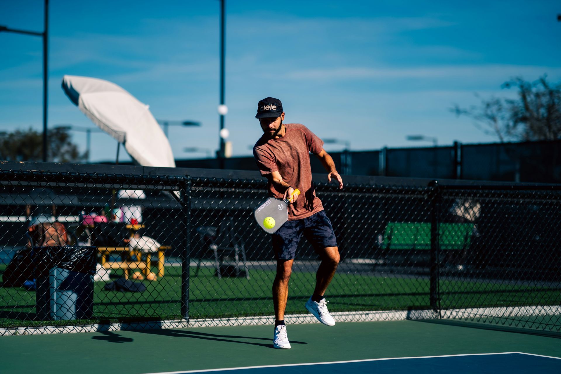 Man playing pickleball outdoors, hitting the ball. Blue court, sunny day.