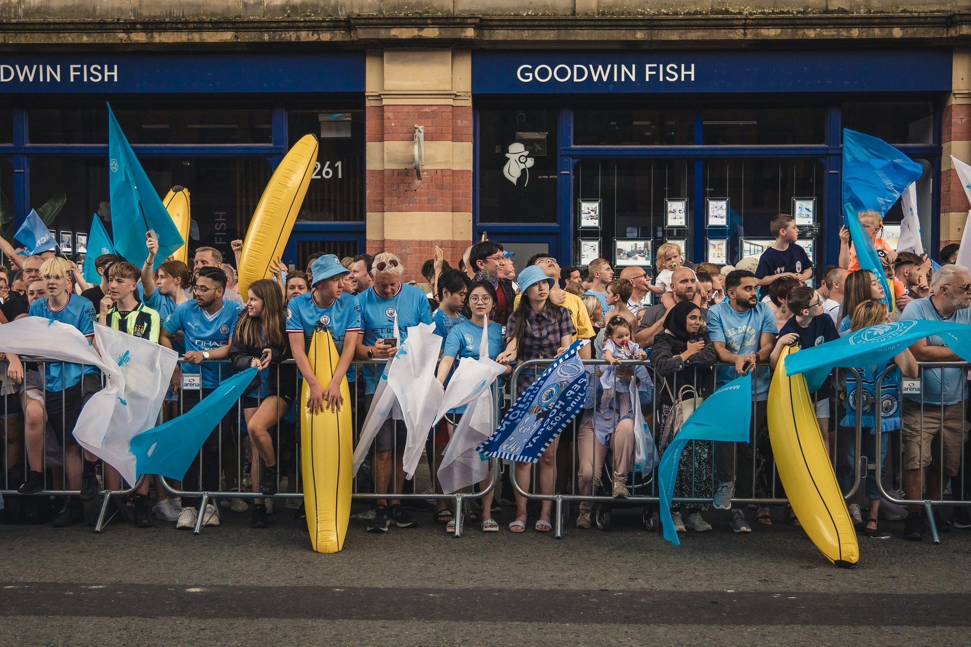 A crowd of people are standing in front of a building that says goodwin fish
