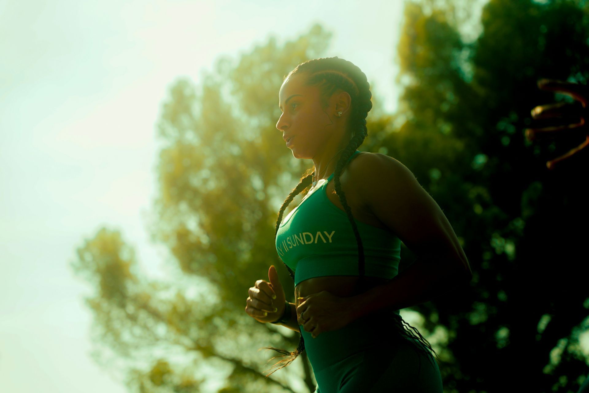 A woman is running in the woods on a sunny day.