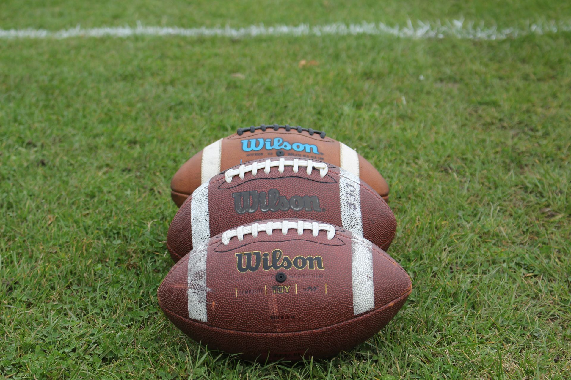 Three wilson footballs are sitting on top of each other on a field.