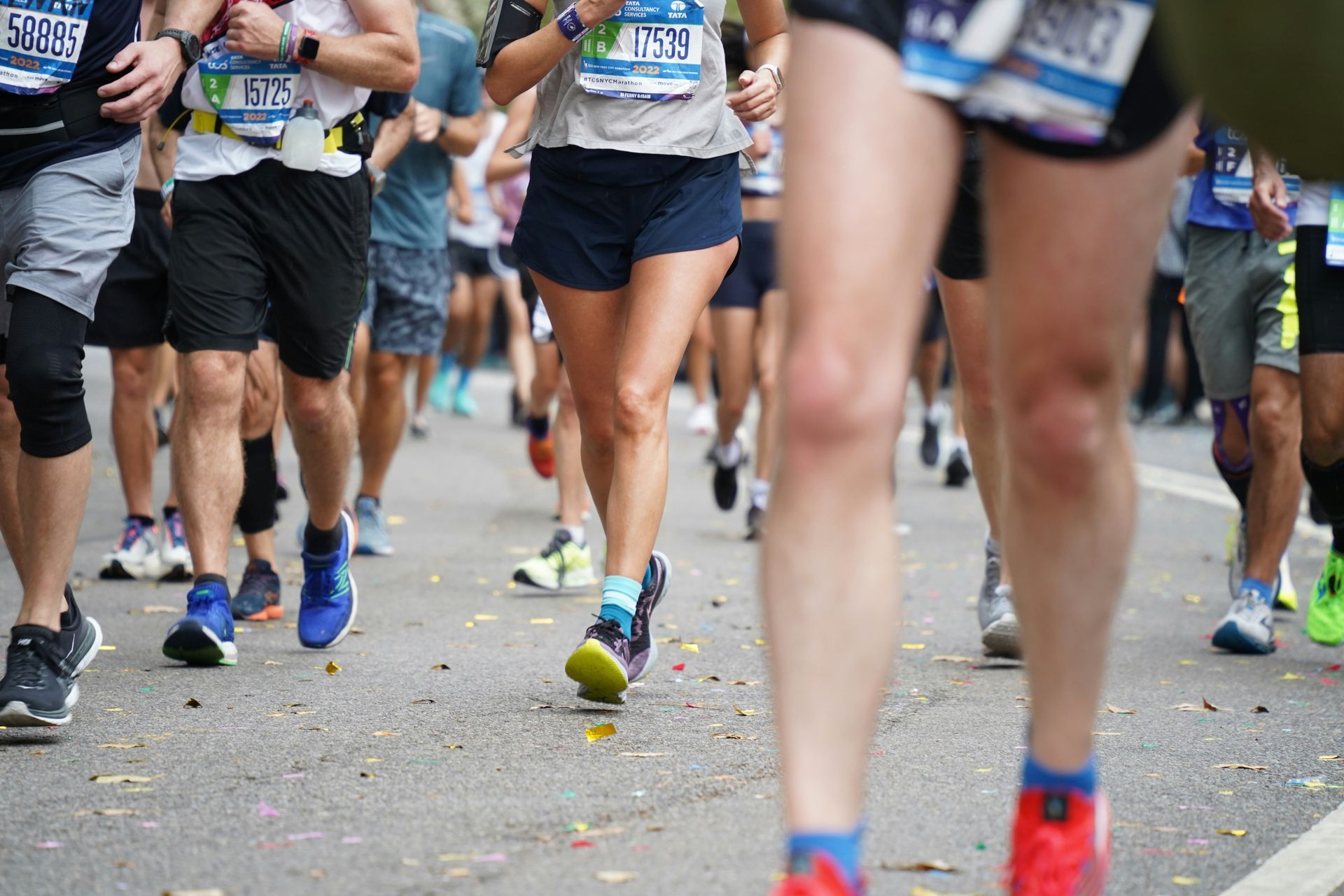 Runners in a marathon, legs in motion on a gray street. Many legs and feet, colorful shoes.