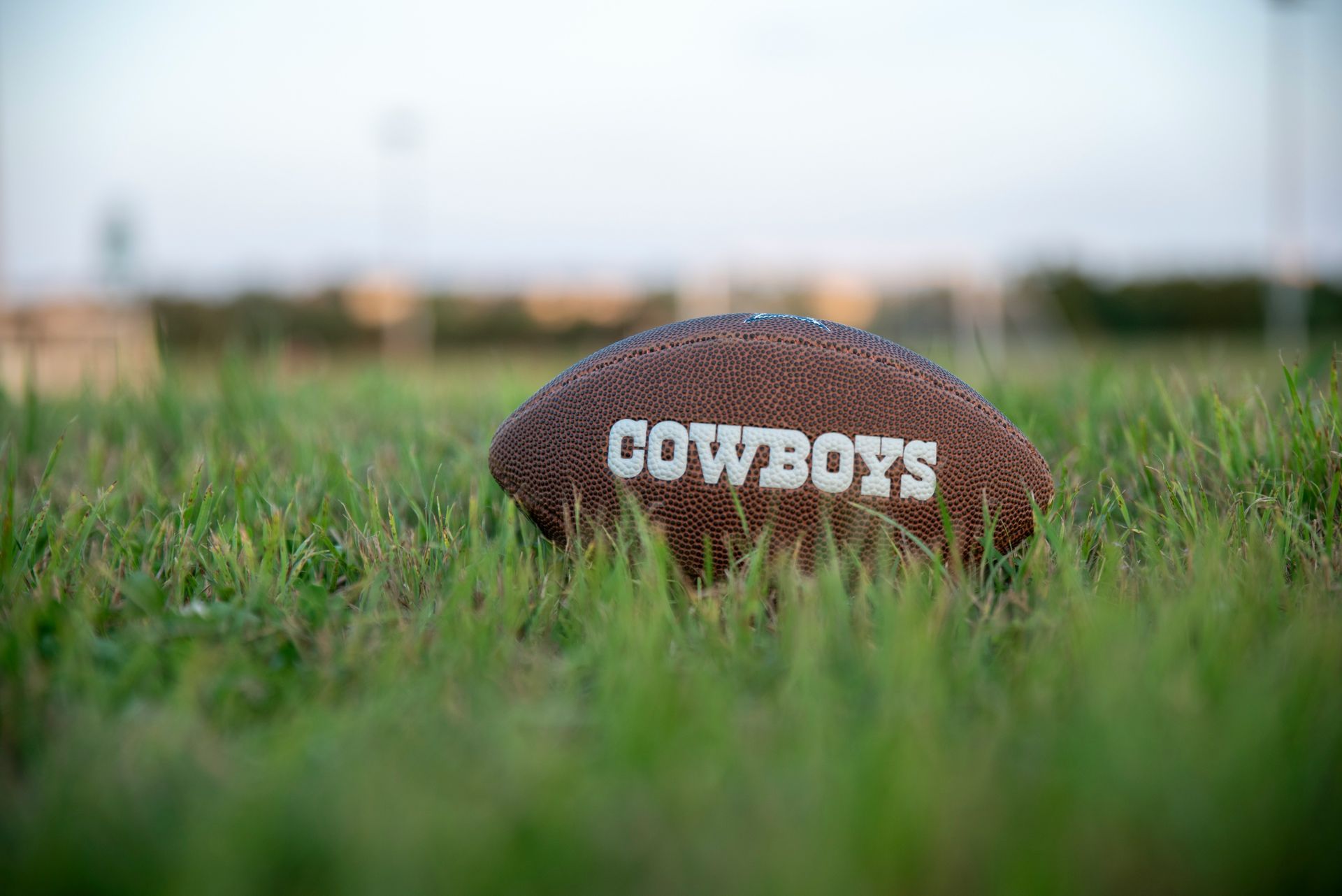 A cowboys football is sitting on top of a lush green field.