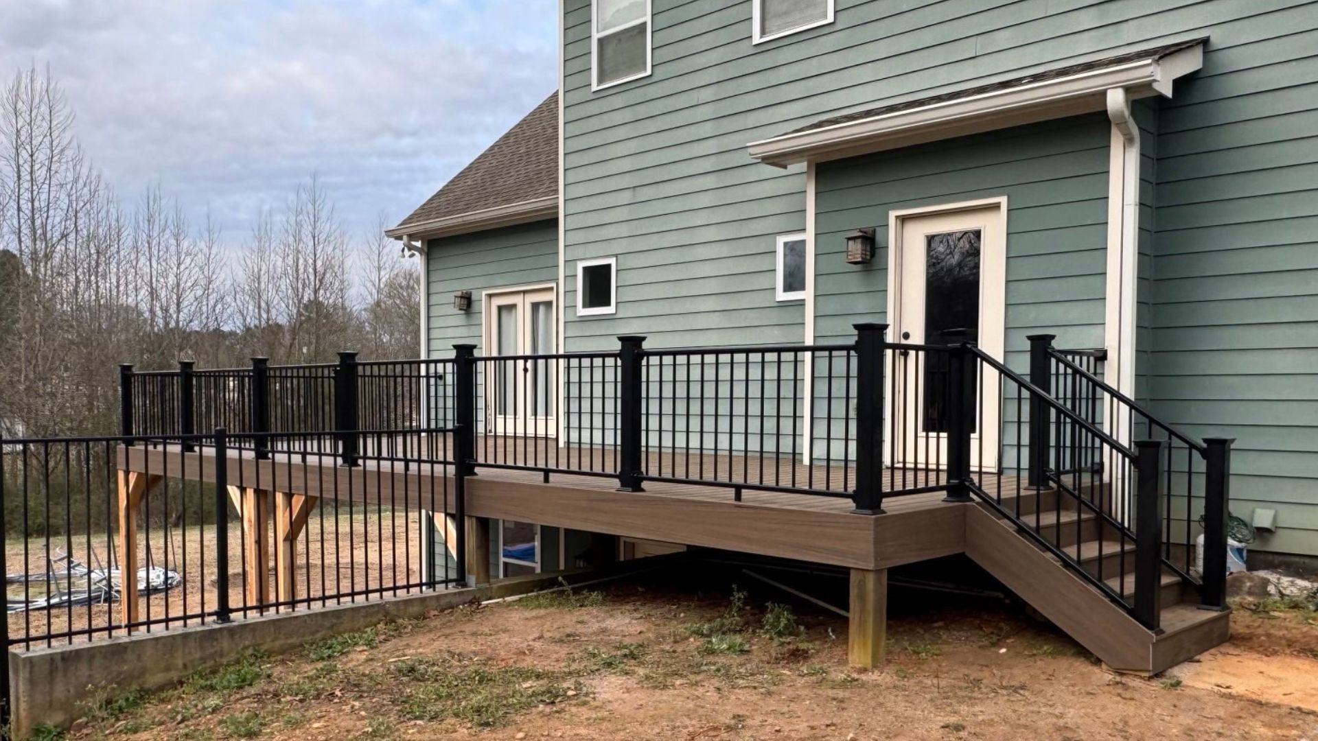 A composite deck with black railings adjoins a teal house with a door and windows.