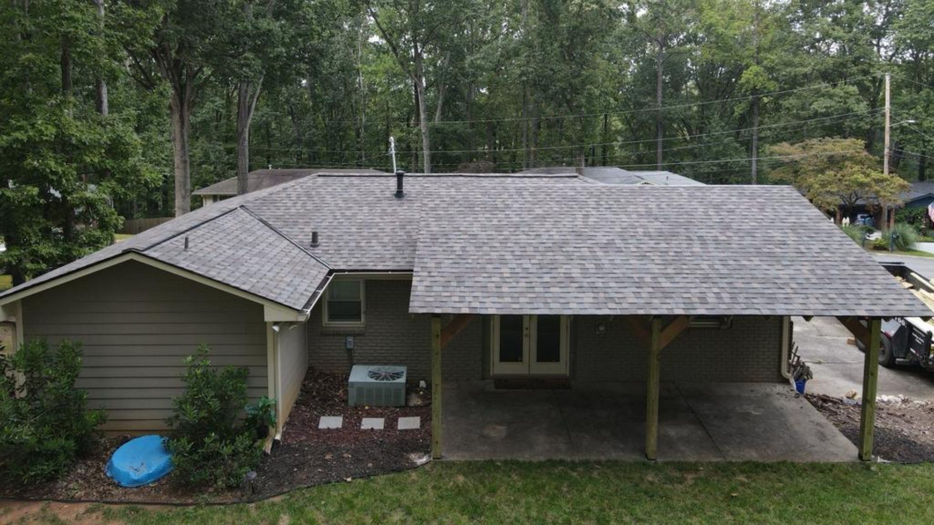 House with gray roof, covered patio, and green siding, set in a yard with trees.