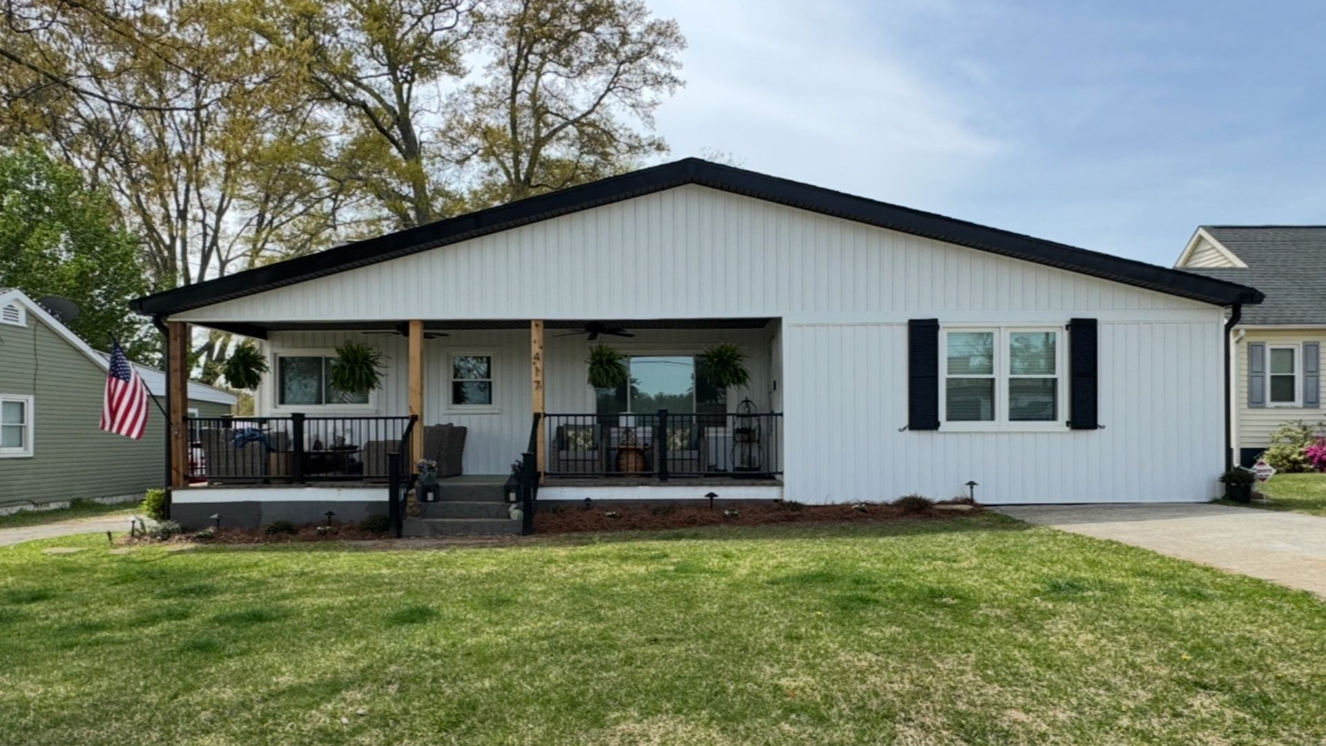 White house with black trim and front porch; green grass and blue sky.