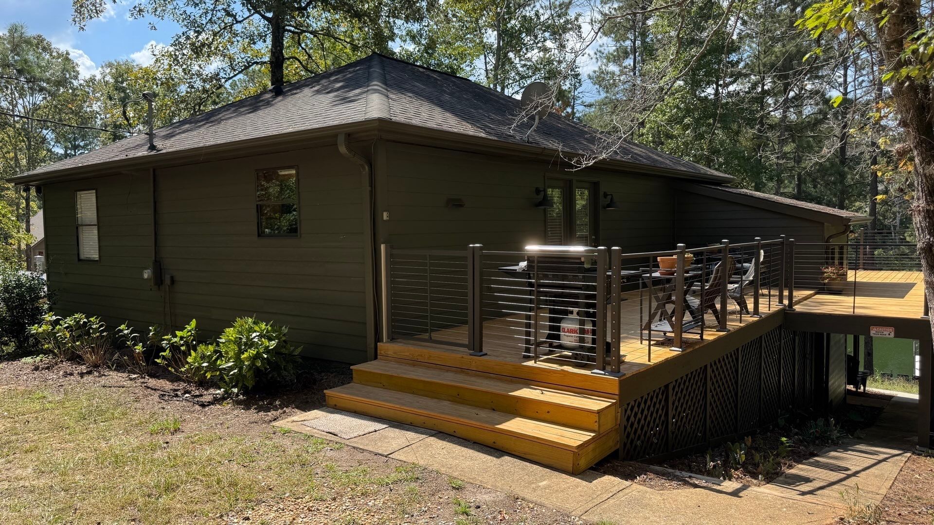 Olive green house with wood deck and steps in a wooded setting.