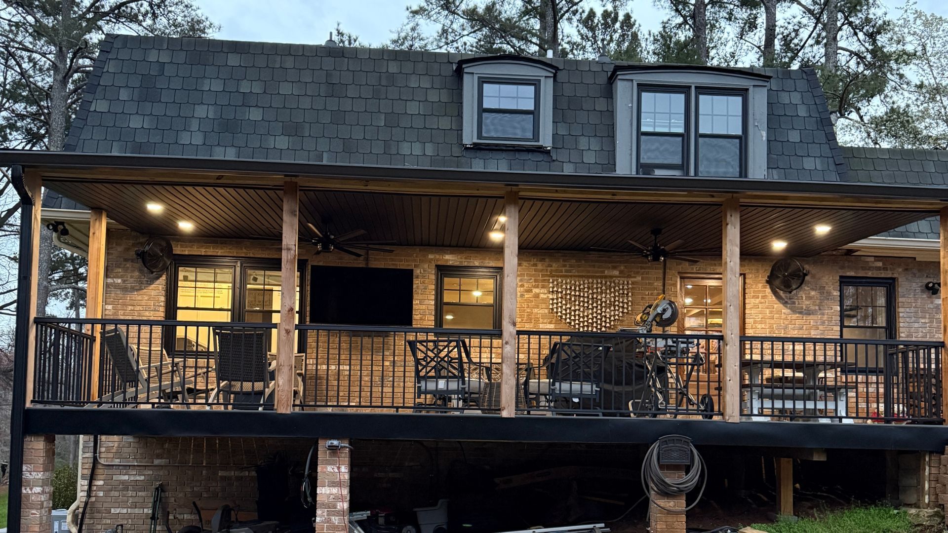 A two-story brick house with a covered deck, lit with overhead lights, and seating.