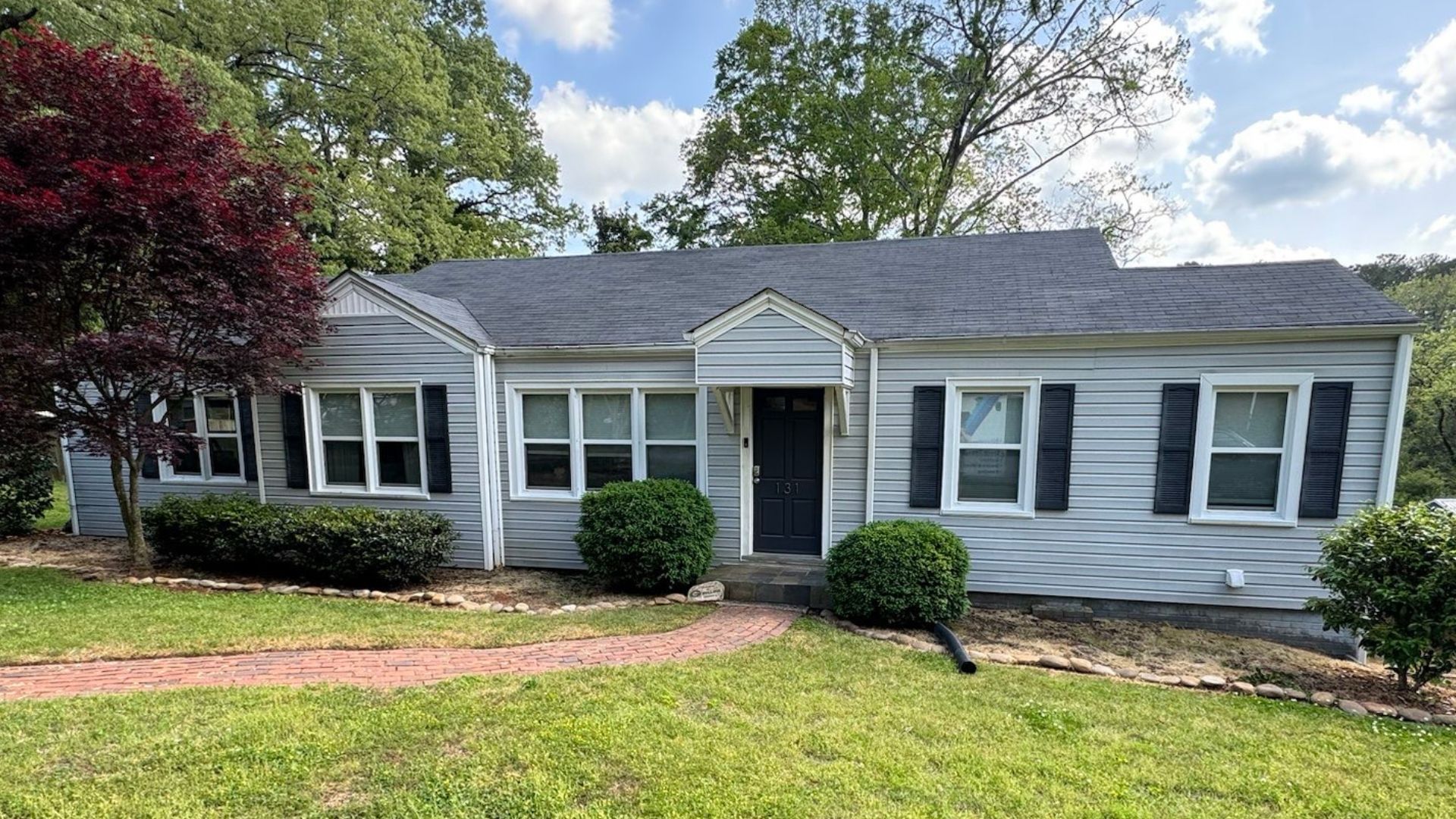 Single-story gray house with white trim, black shutters, a front lawn, and a centered entryway.