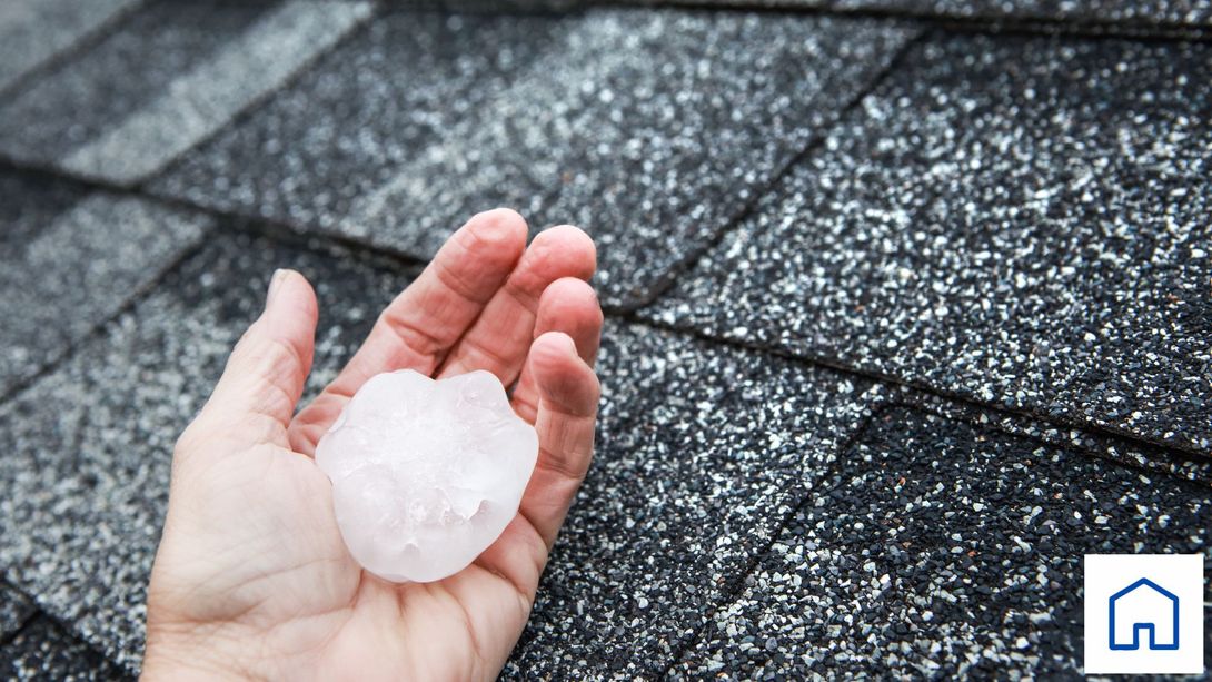 A person is holding a piece of hail in their hand in front of a roof in Carrollton Ga