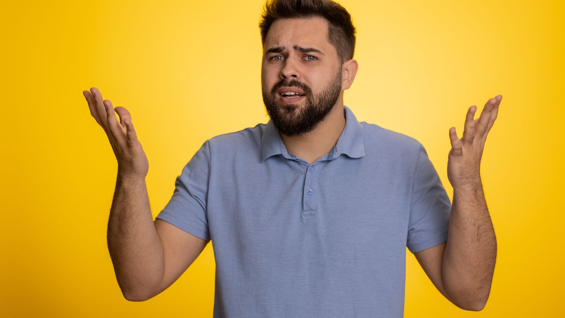 A man with a beard is making a funny face with his hands in the air.