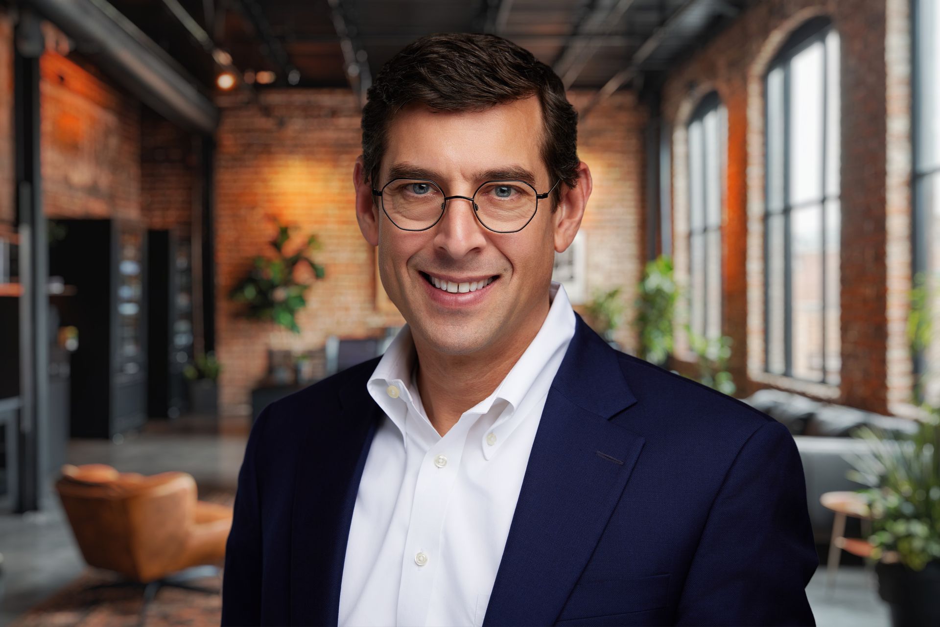 A man wearing glasses and a blue suit is smiling
