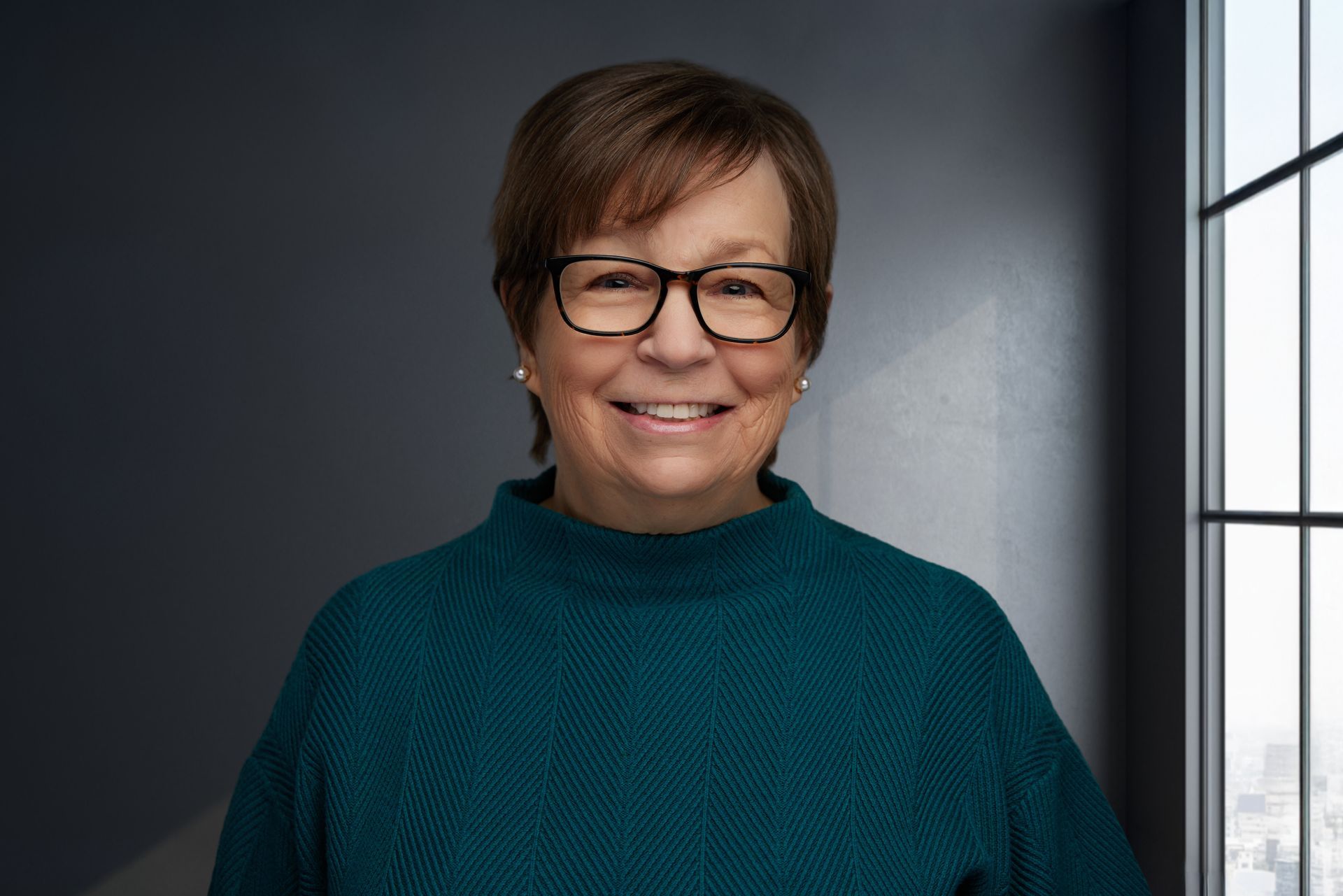 A woman with blonde hair is smiling and wearing a black jacket.