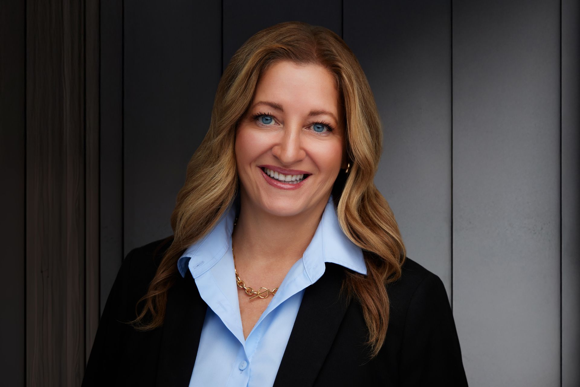 A woman wearing a pink jacket and a white shirt is smiling for the camera.