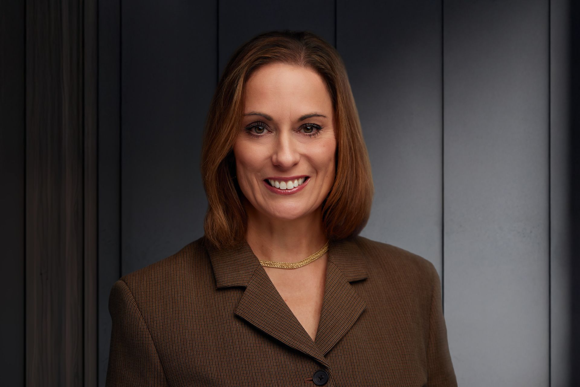 A woman wearing a black jacket and a pink scarf is smiling for the camera.