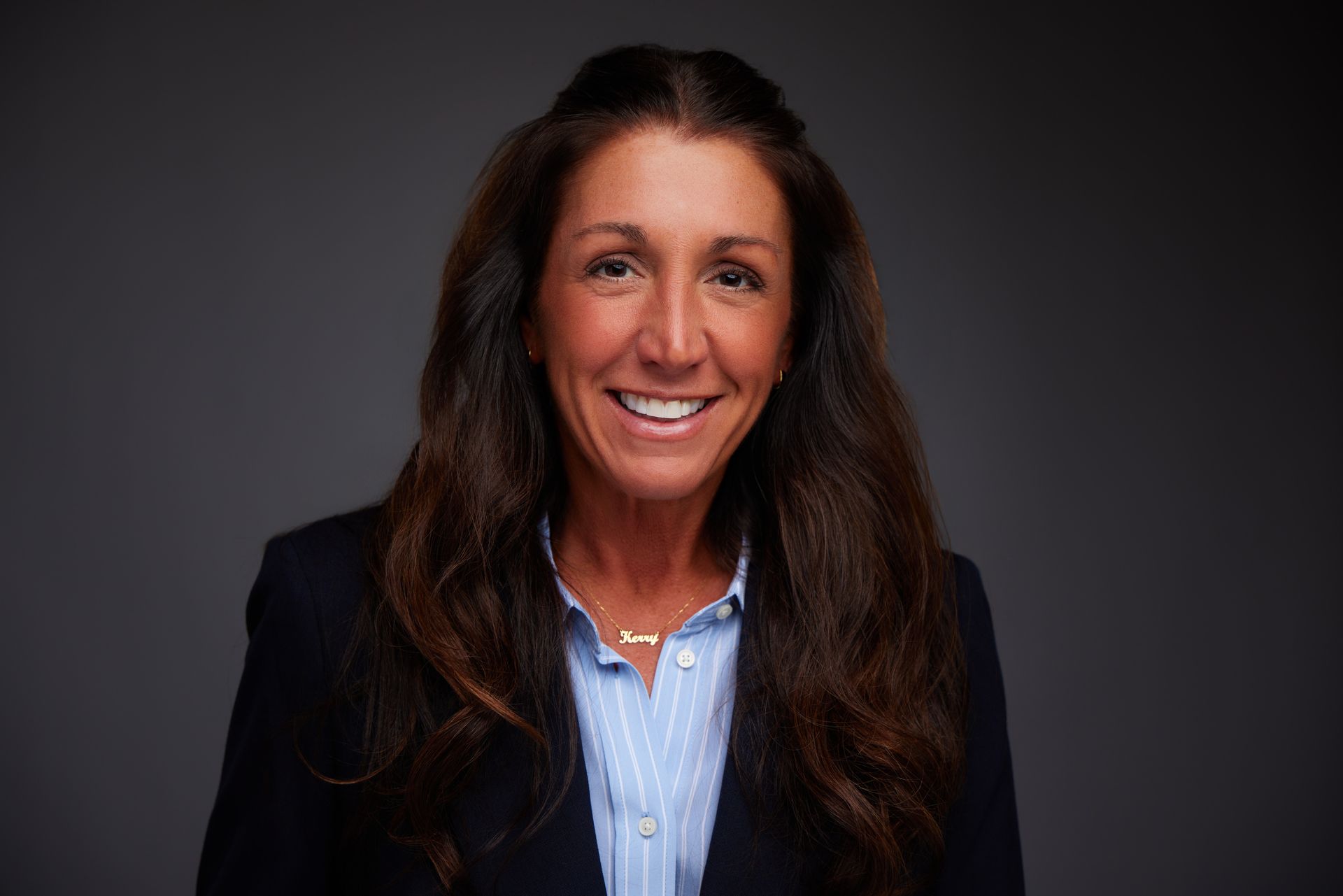A woman wearing a black jacket and earrings smiles for the camera