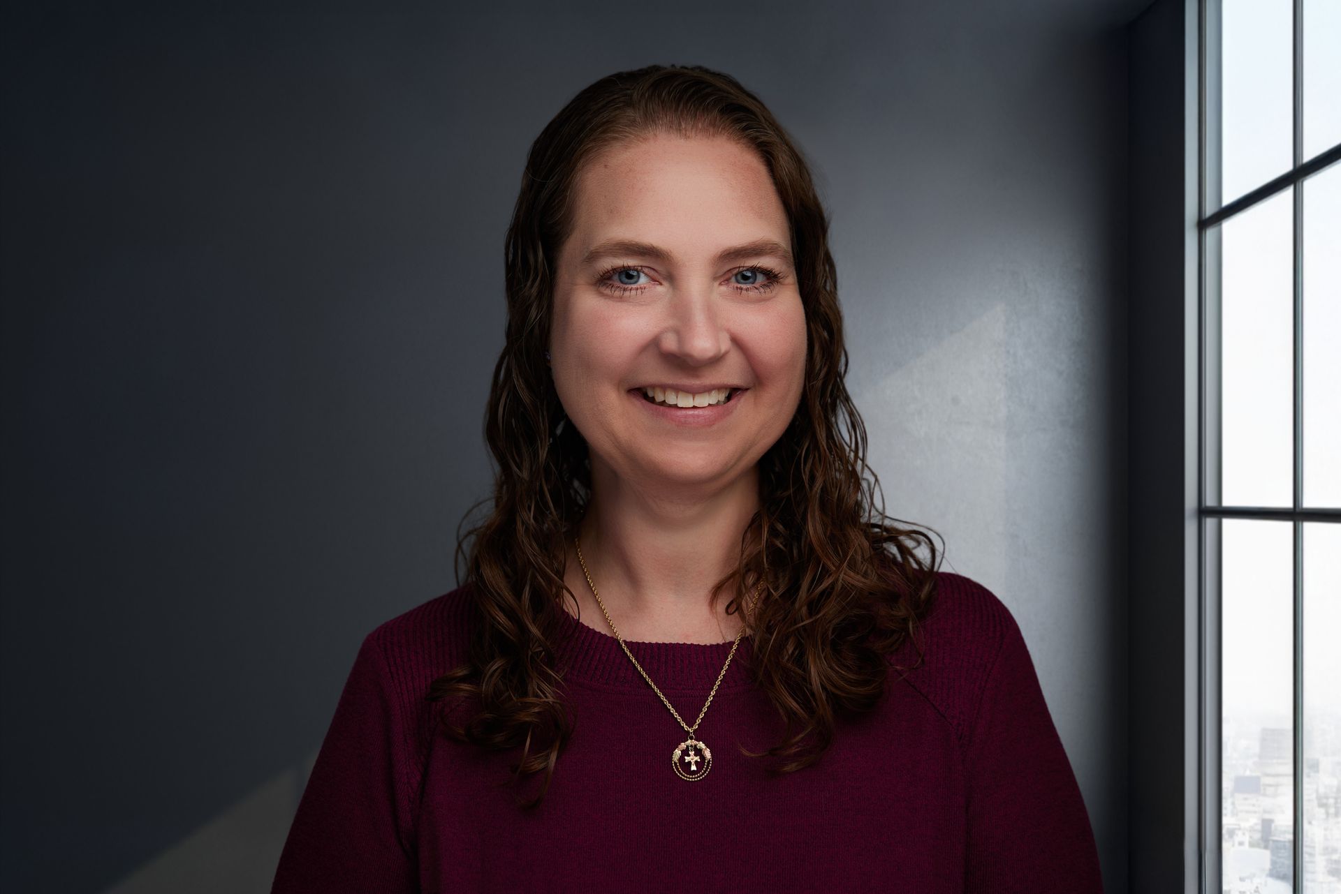 A woman wearing a brown sweater and a necklace is smiling for the camera.