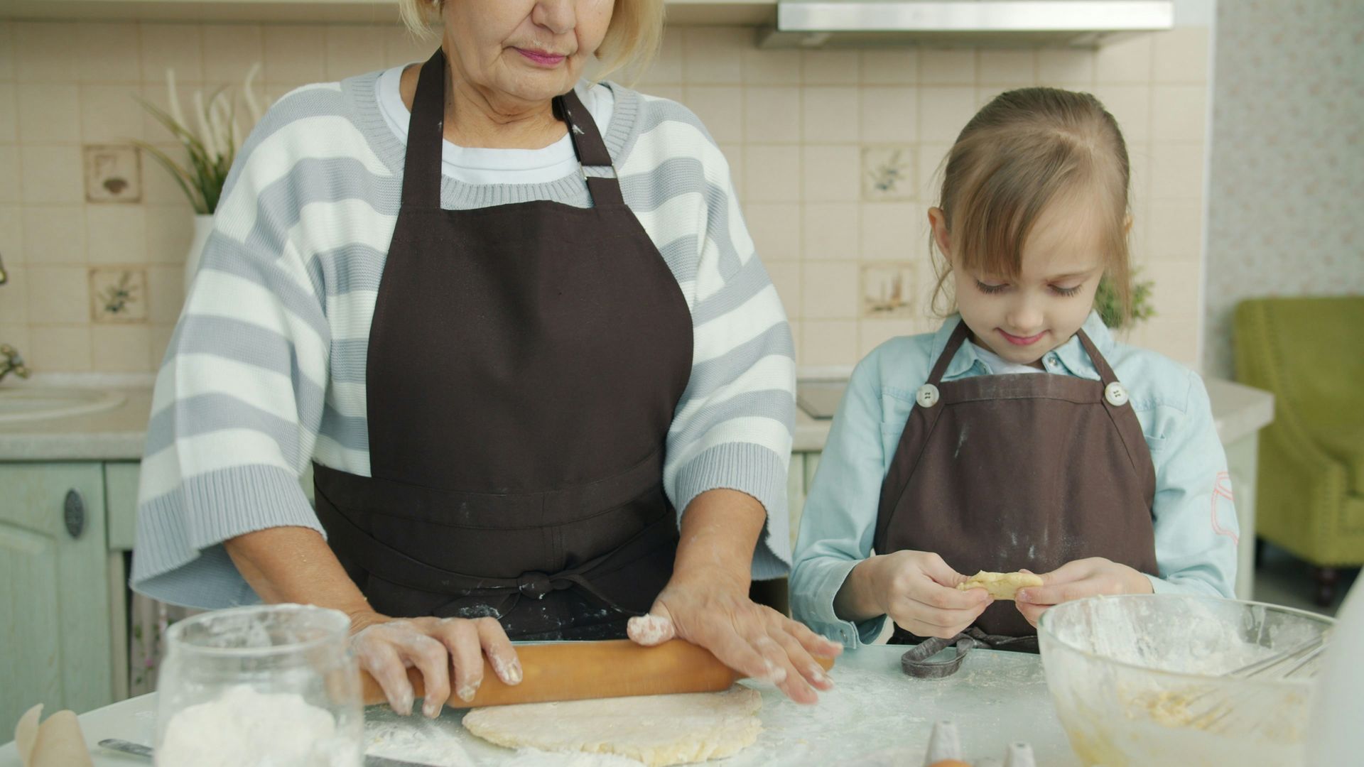 Grandmother and granddaughter baking together in a kitchen; rolling dough and filling pastries.
