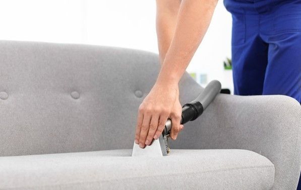 Person vacuuming a gray sofa with a handheld upholstery attachment. Person vacuuming a gray sofa with a handheld upholstery attachment.