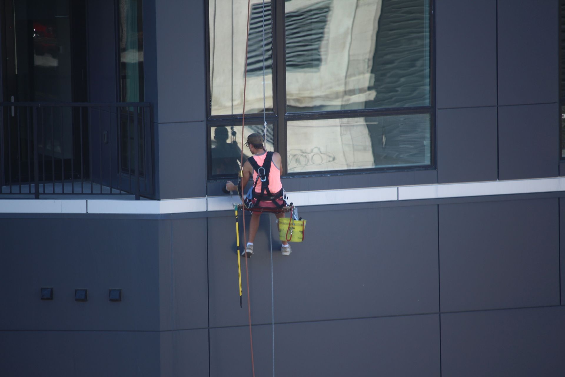 A man is sitting on the side of a building cleaning windows.