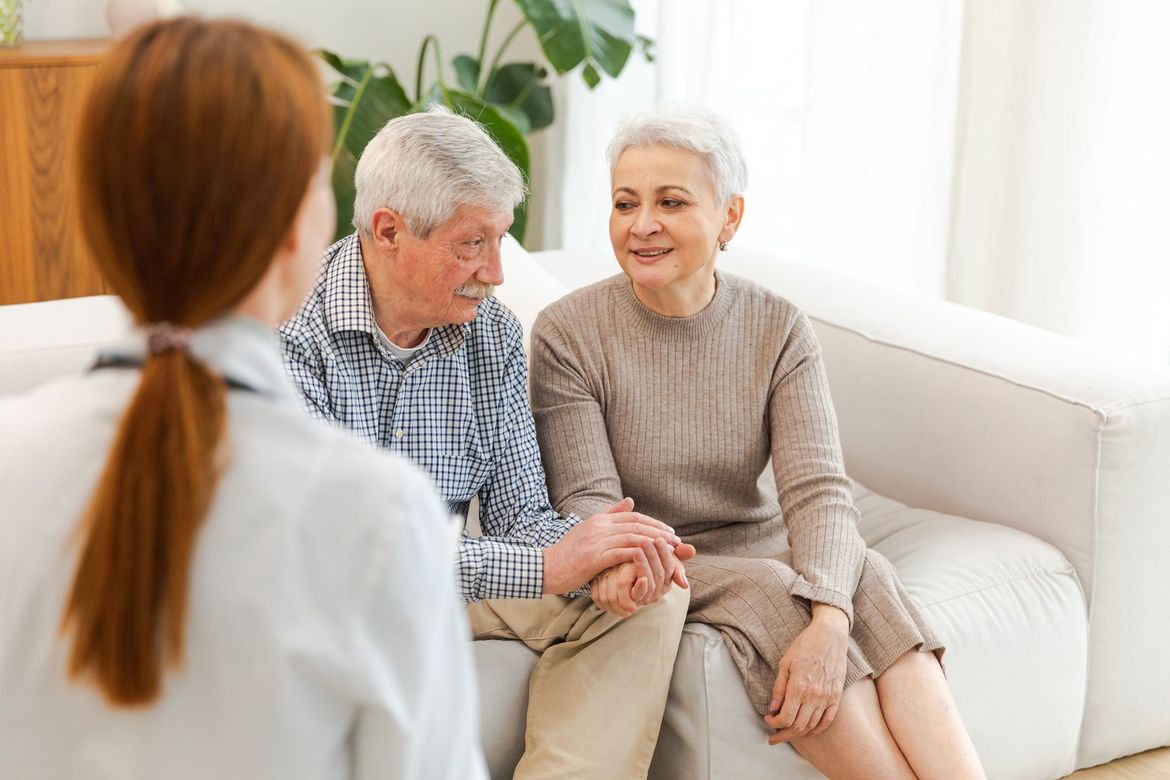 An elderly couple is sitting on a couch talking to a doctor.