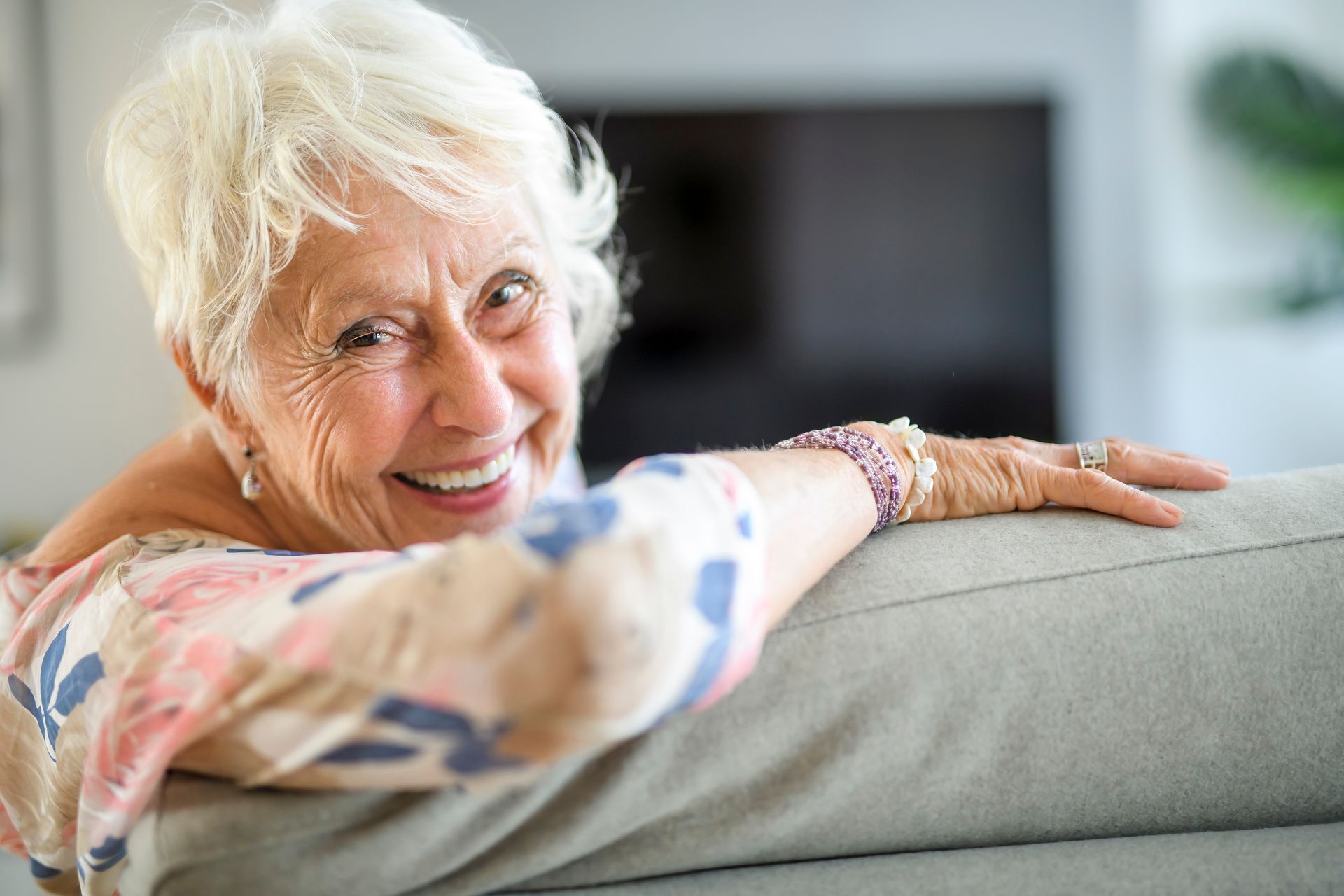 An elderly woman is sitting on a couch and smiling.