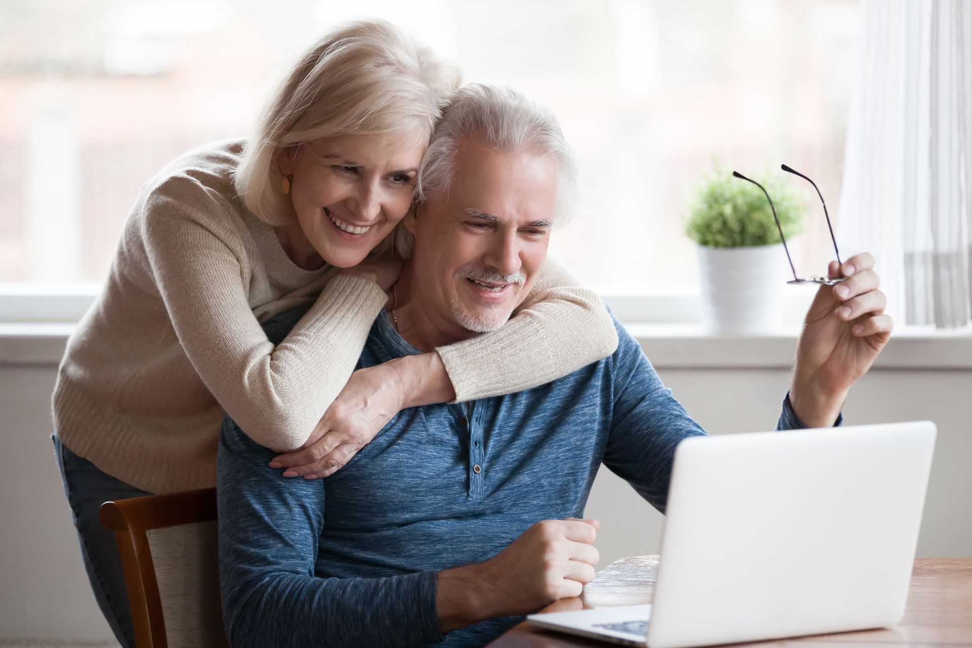 A woman is hugging a man while he uses a laptop computer.