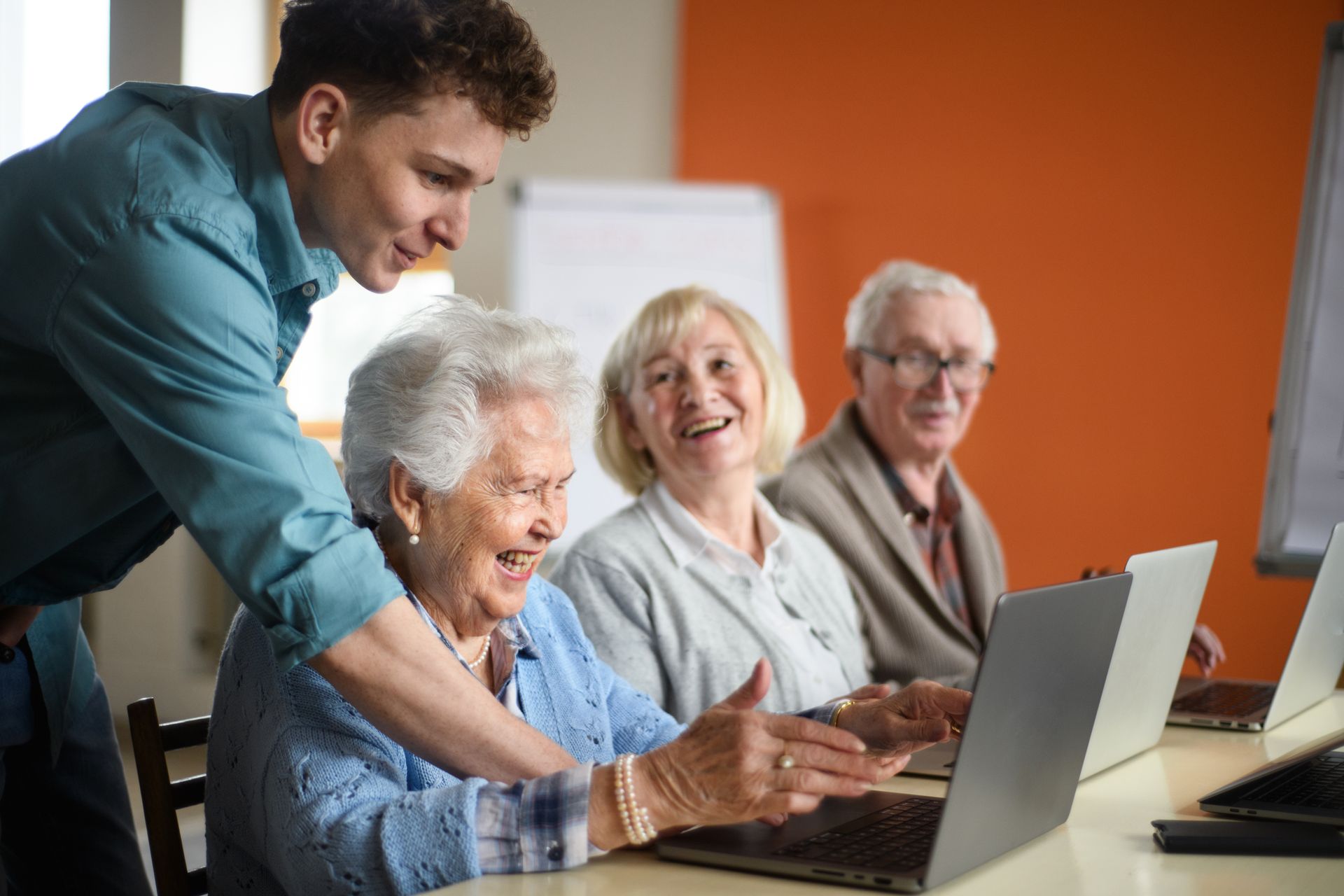 A group of elderly people are sitting at a table using laptops.