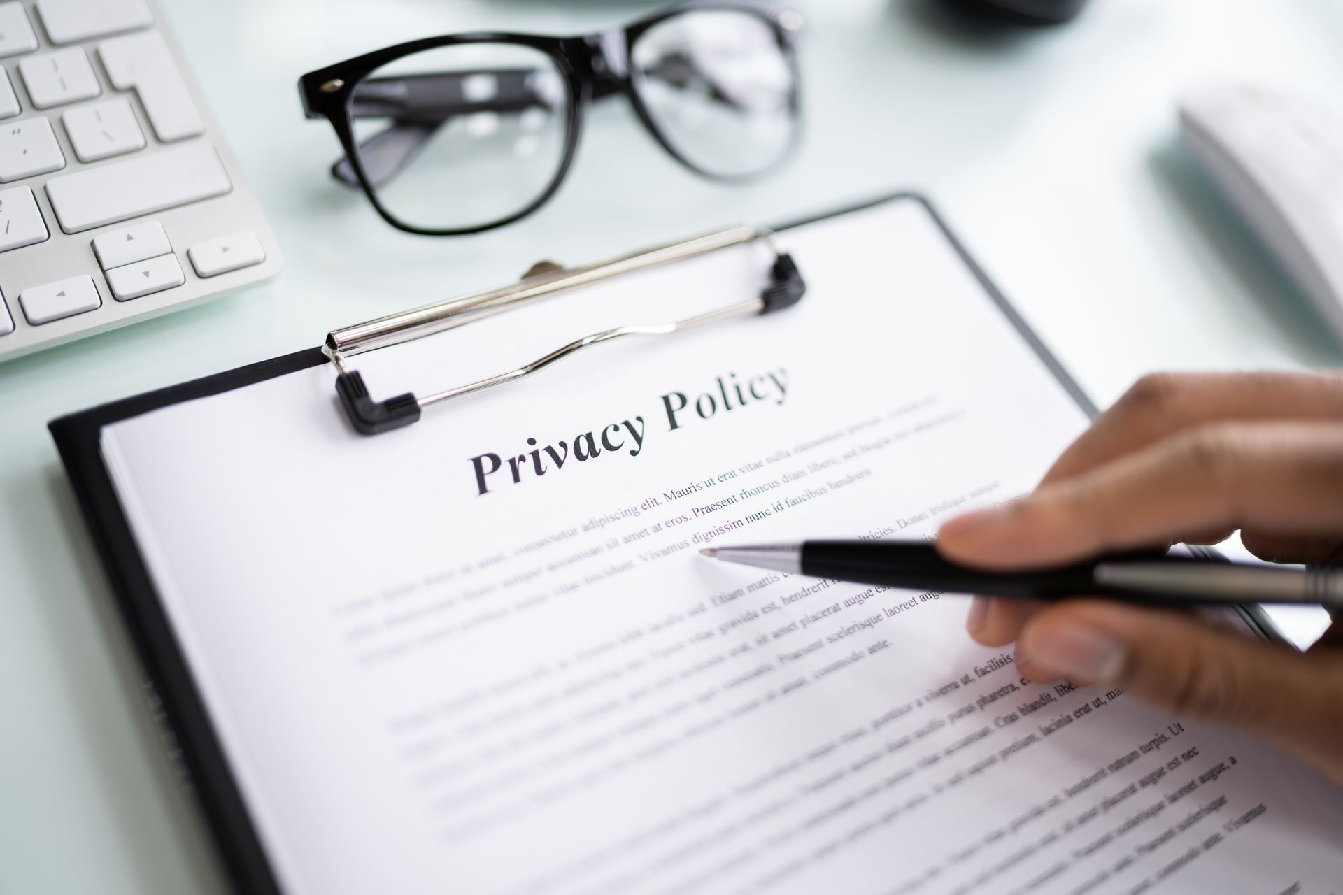 A person is holding a pen over a privacy policy on a clipboard.