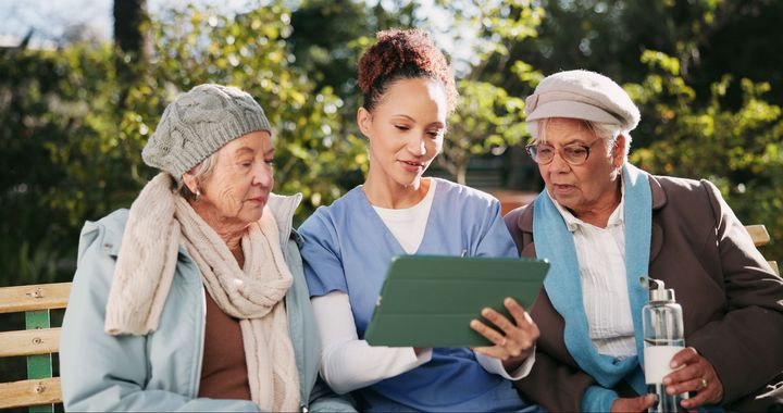 A nurse is teaching two elderly women how to use a tablet computer.