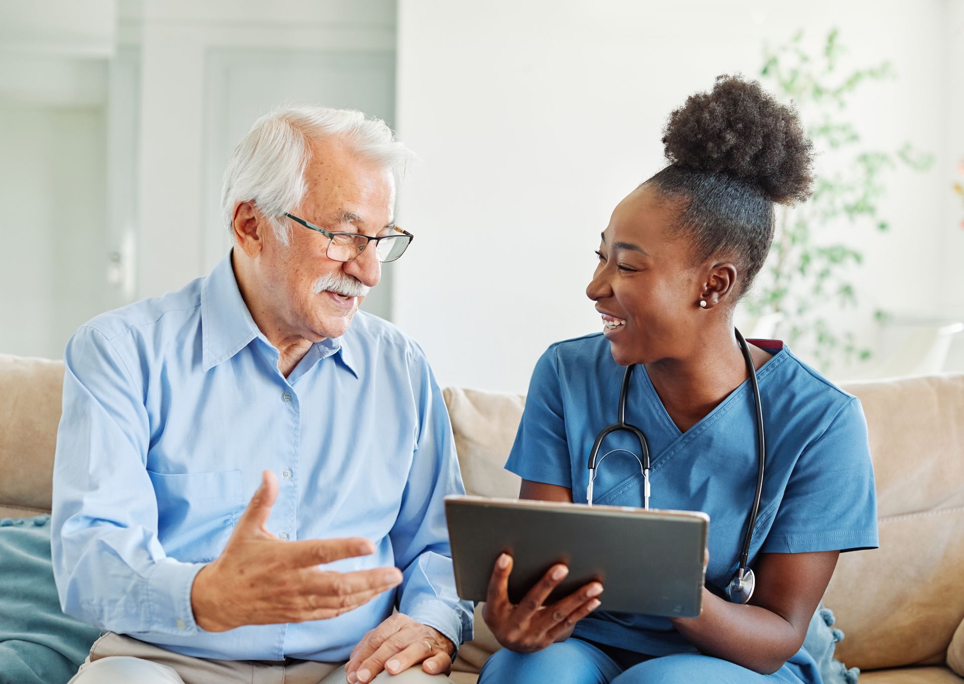 A nurse is talking to an elderly man while looking at a tablet.