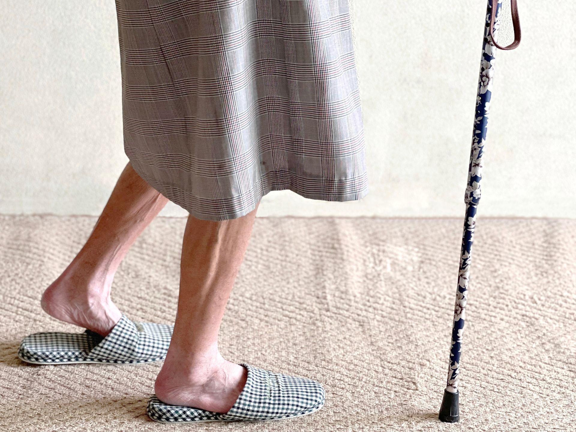 A woman wearing slippers and a cane is walking on a carpet.