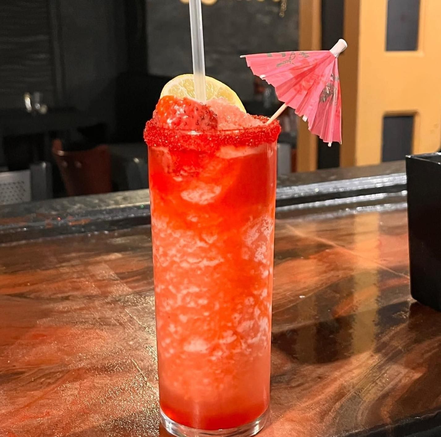 Strawberry cocktail in a tall glass, garnished with a lemon slice, strawberry, and a red rim.