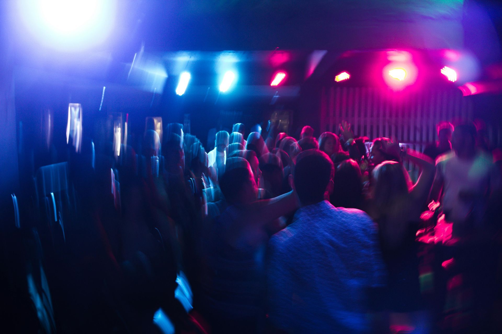 People dancing in a nightclub with blue and pink neon lights.