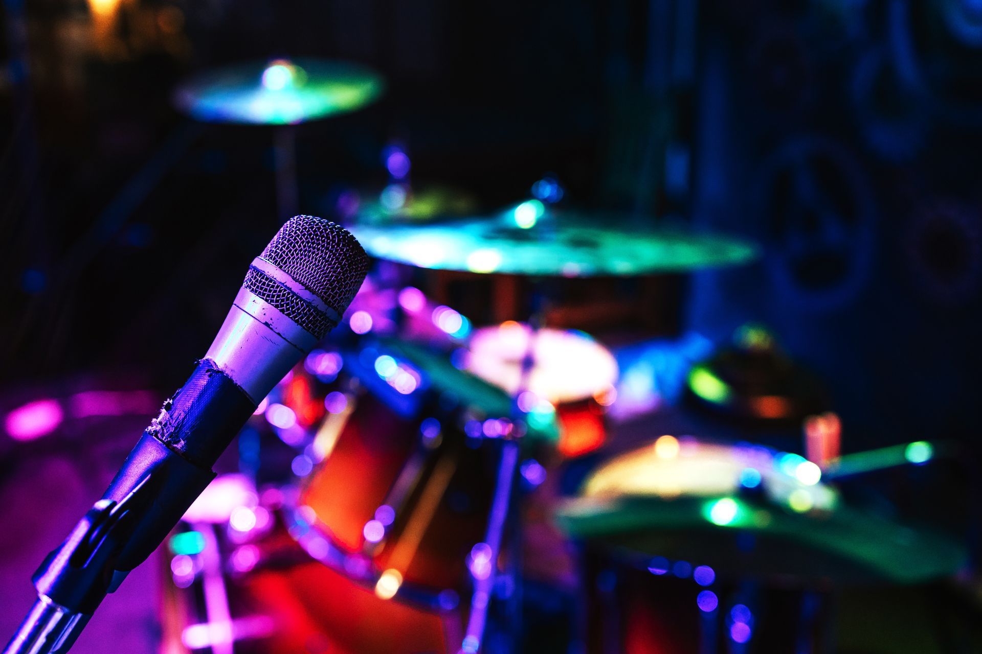 Microphone in the foreground, drum set illuminated by colorful stage lights in the background.