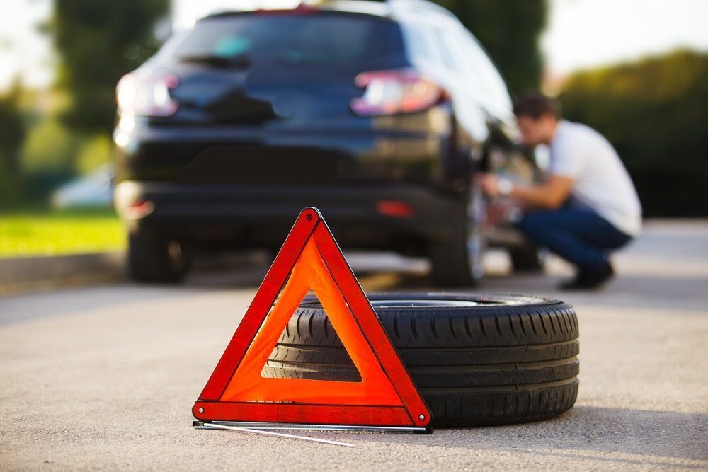 A Man is Changing a Tire on a Car on the Side of the Road — Stamford Tyres In Ballarat Central, VIC