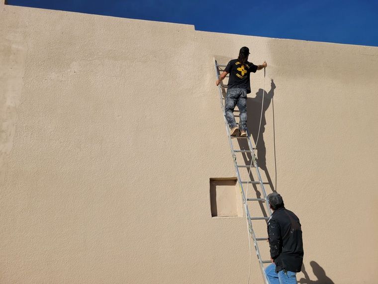 Two men are painting a wall and one is on a ladder