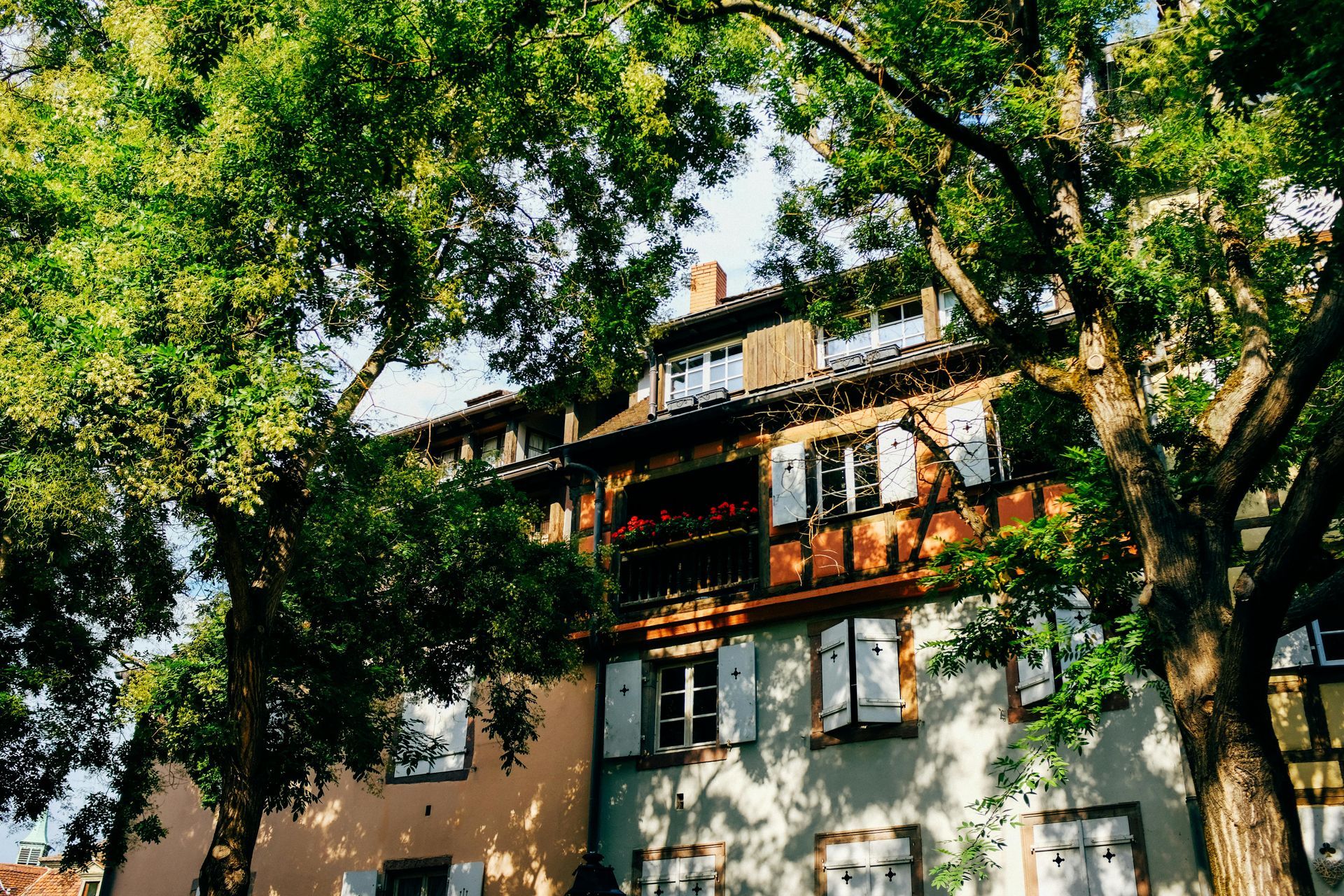 A house with a balcony is surrounded by trees on a sunny day.