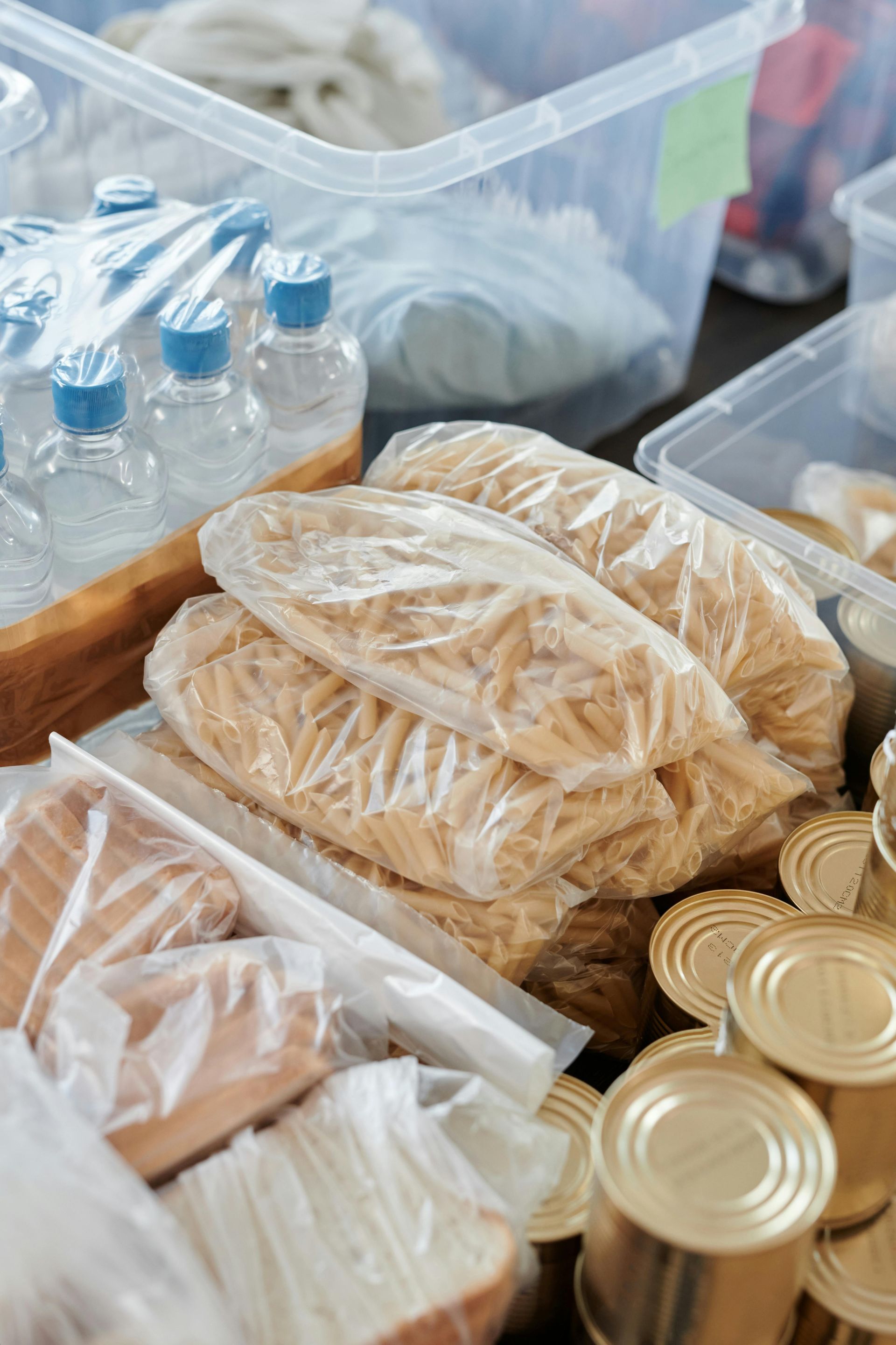 A table topped with bags of noodles , cans of food and water bottles.