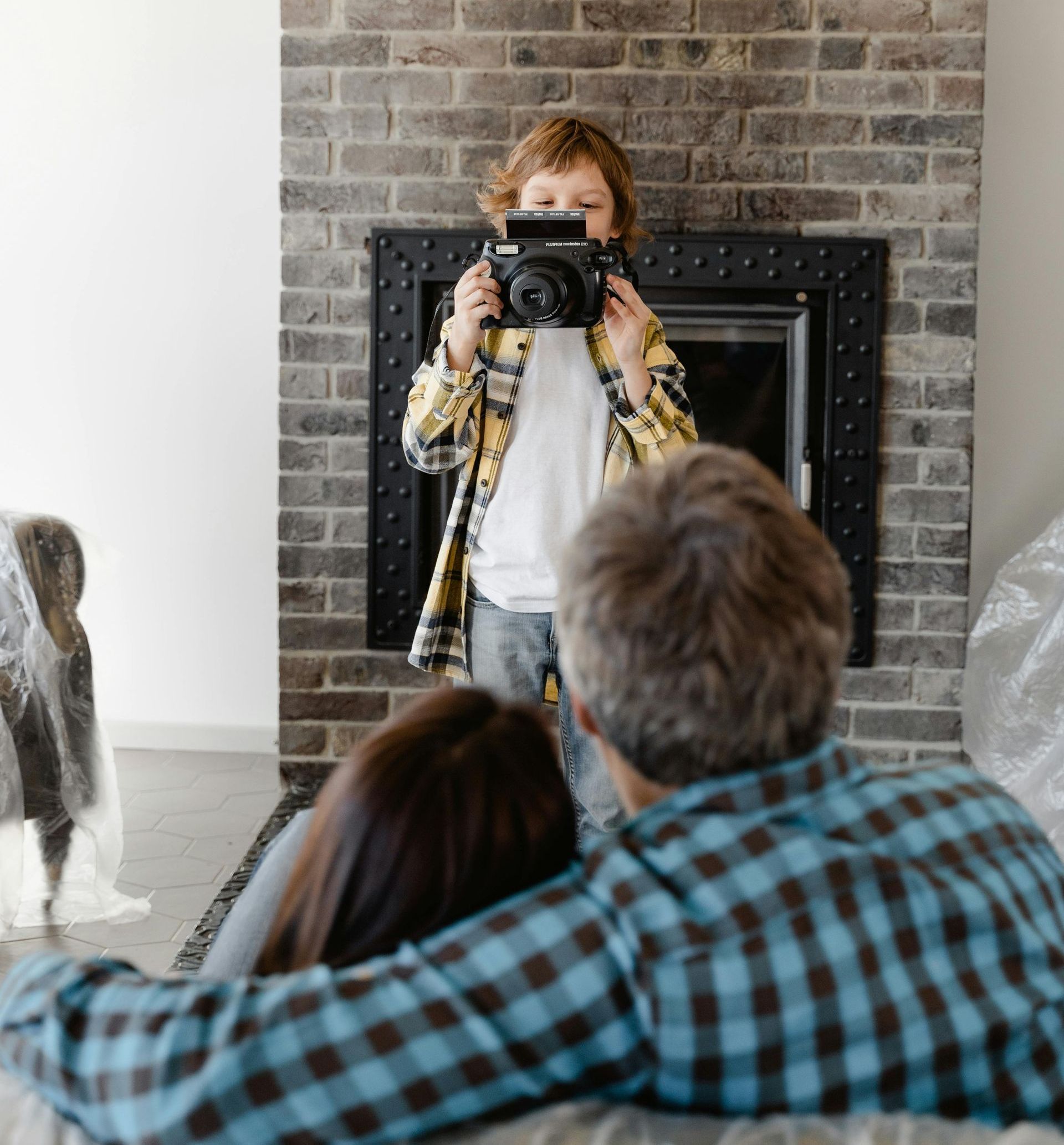 A boy is taking a picture of a family in front of a fireplace.