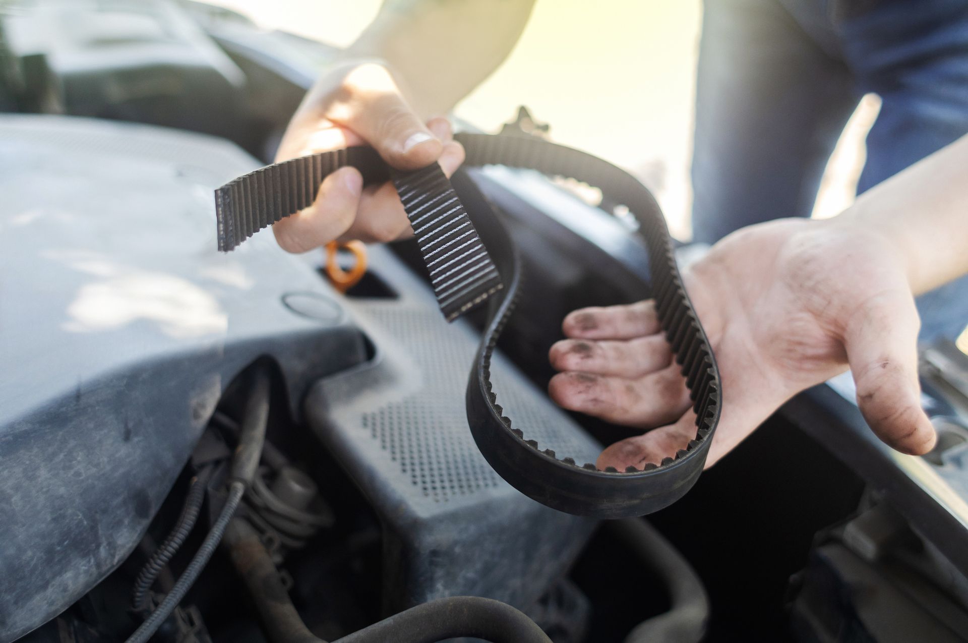 A person is holding a belt in front of a car engine.