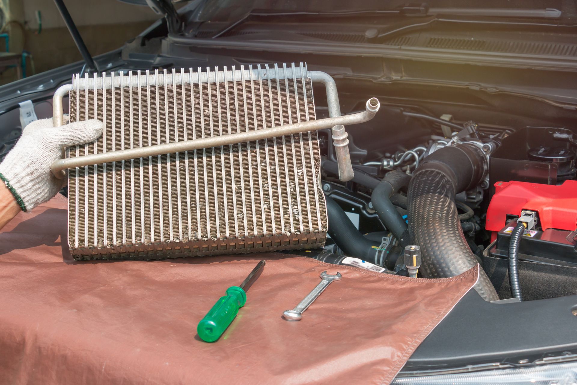 A person is holding a radiator next to a car engine.