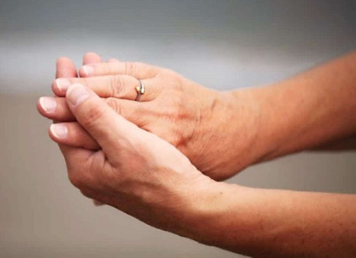 Een vrouw met een trouwring aan haar vinger houdt haar handen bij elkaar.