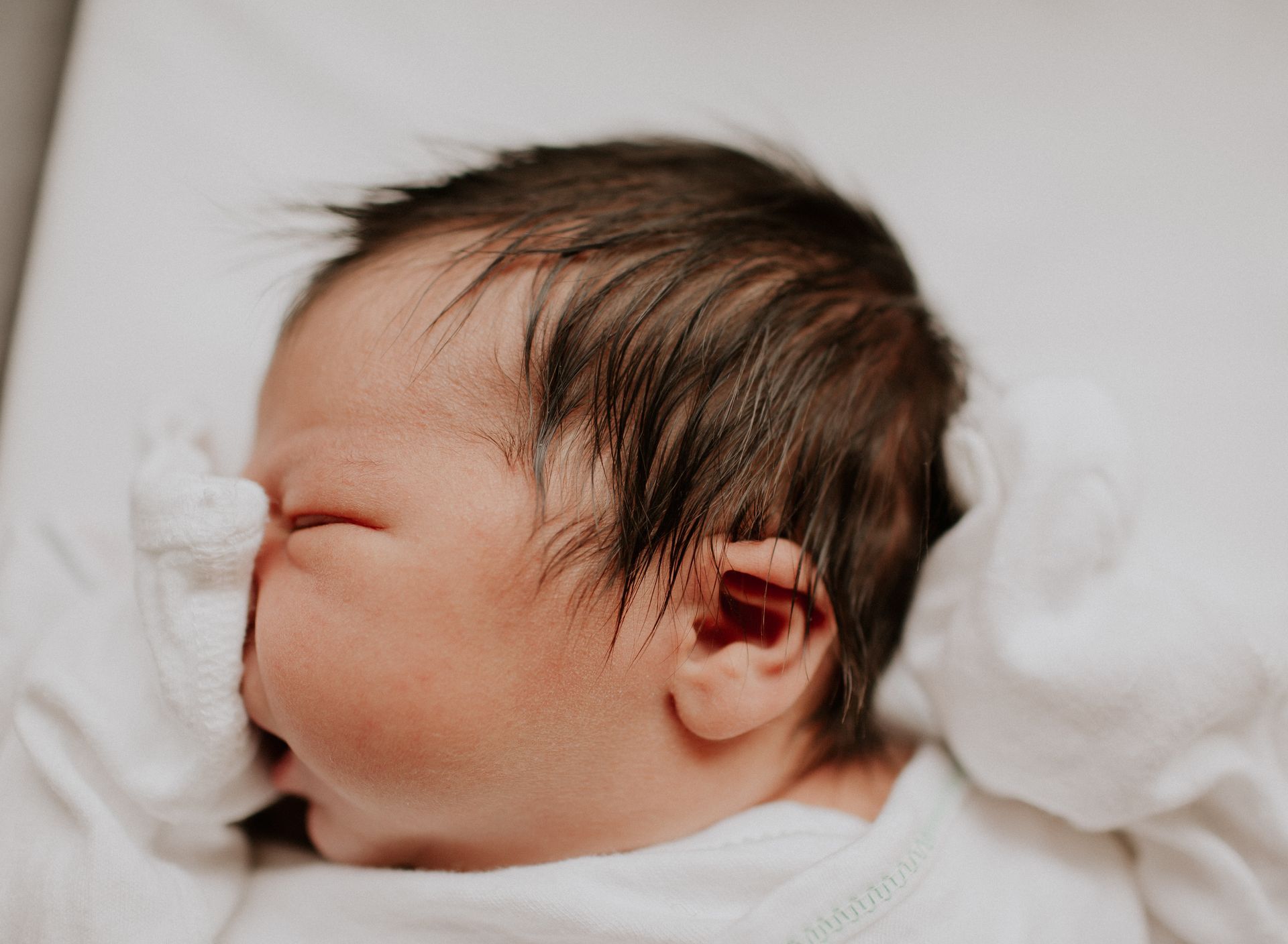 Newborn baby with dark hair, sleeping, wrapped in white.