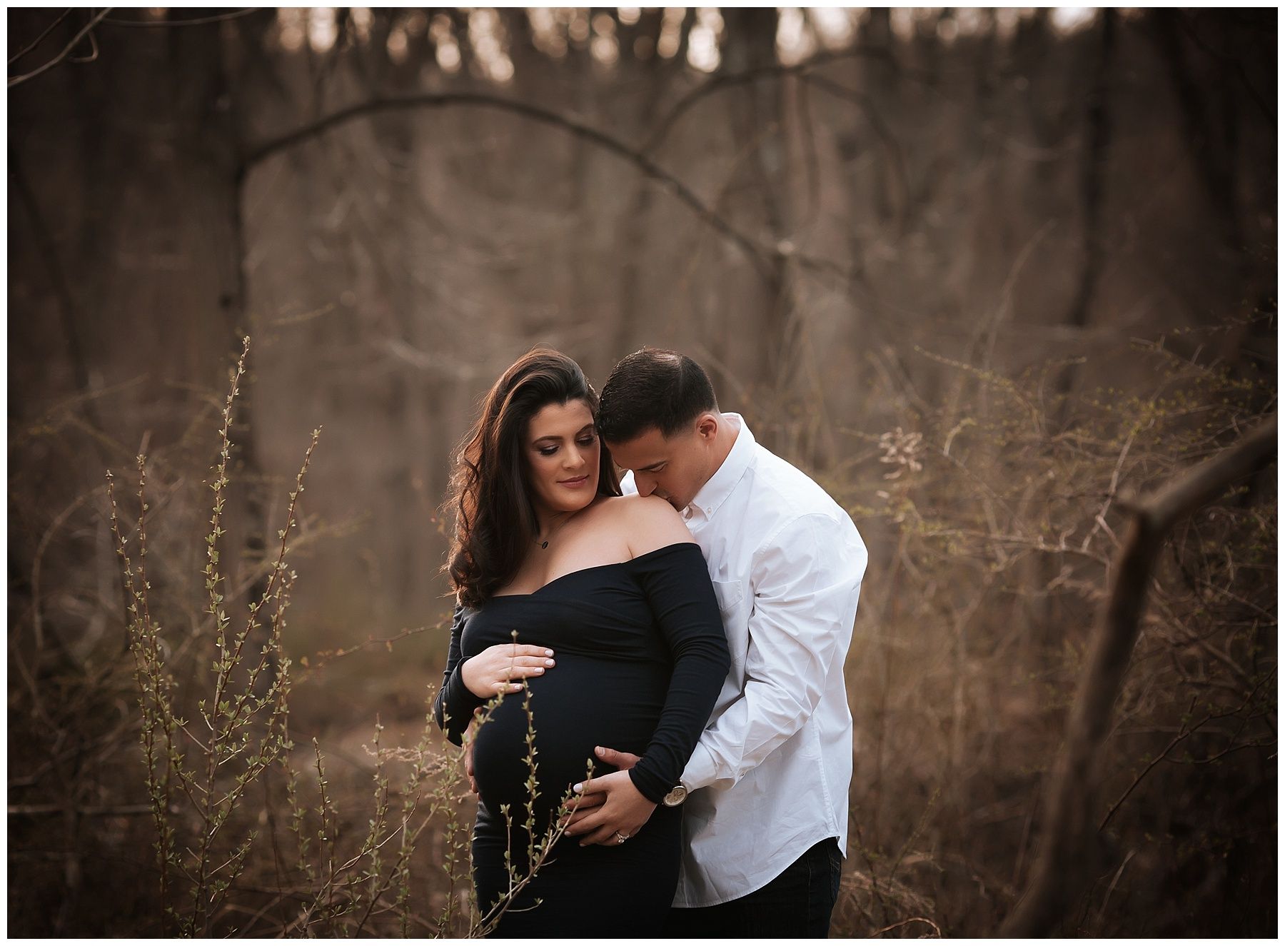 A man is hugging a pregnant woman in a field.