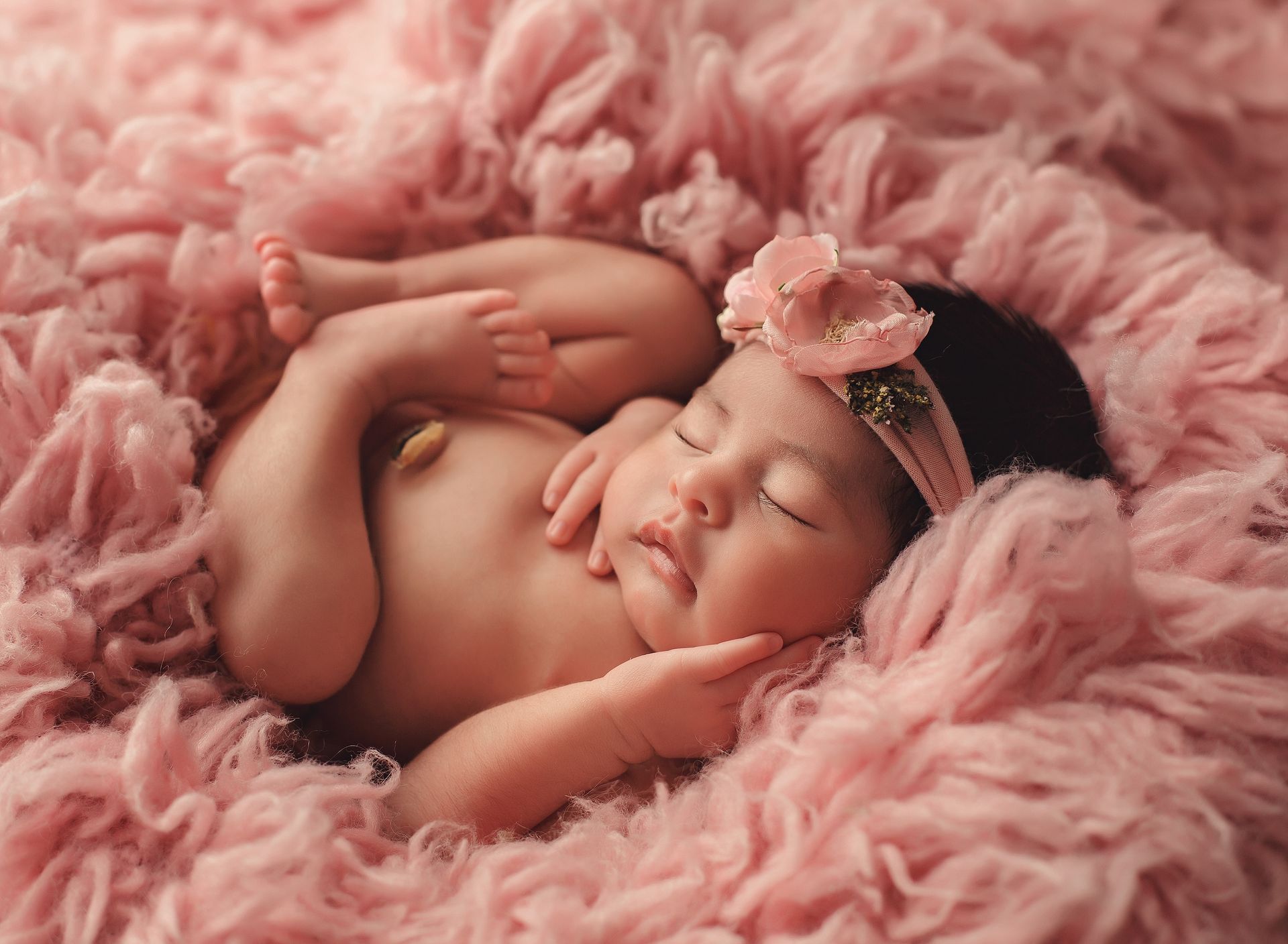 A newborn baby girl is sleeping on a pink blanket.